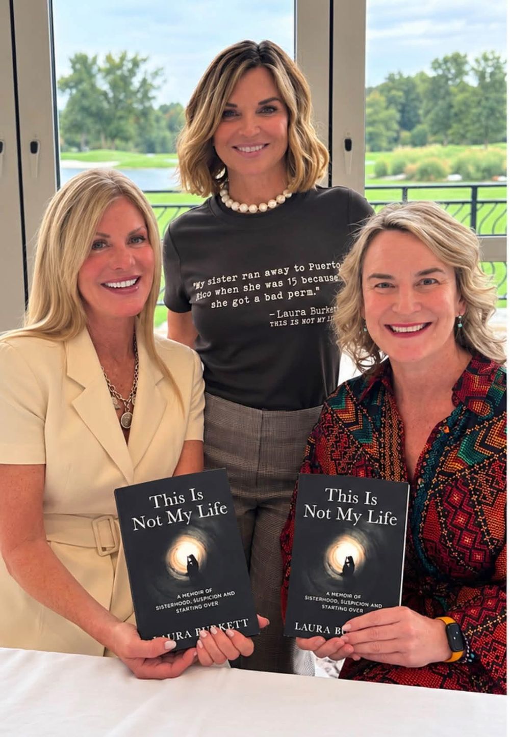Three women smiling for the camera, two holding copies of the book and one wearing a T-shirt with a line from it
